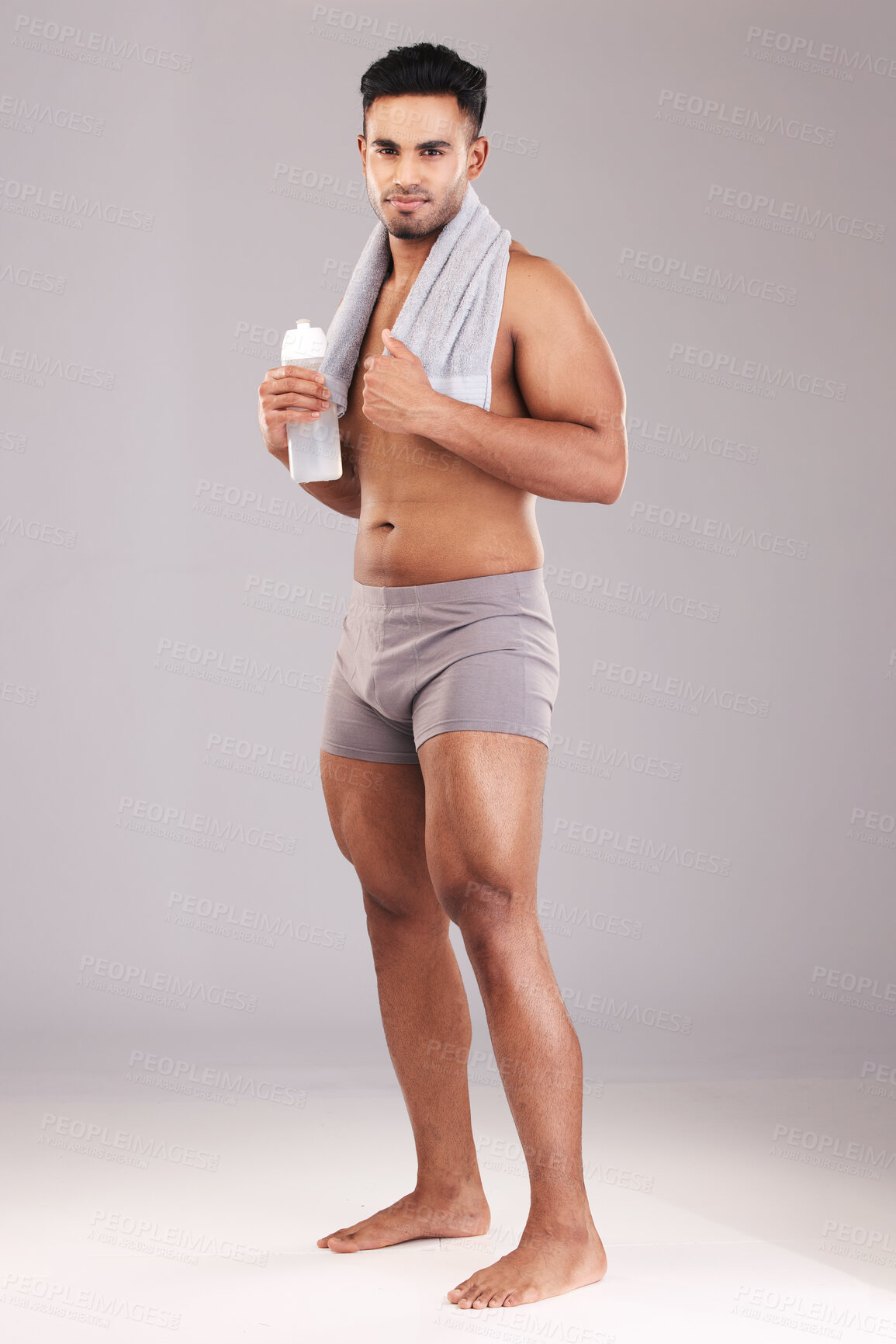 Buy stock photo Portrait, water bottle and man with towel isolated on gray studio background. Fitness, wellness and healthy athletic male from India ready for hydration after training, exercise or workout mock up.