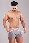 Weightloss, fitness and man with measure tape standing in a studio with a gray background. Health, strong and athlete with a healthy, exercise and diet lifestyle measuring his weight after a workout.