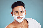 Face, beauty and shaving with a man model in studio on a blue background for wellness or grooming. Portrait, skincare and hair removal with a handsome young male in the bathroom to shave his beard