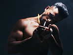 Dark, flame and man lighting a cigarette with a lighter to smoke after a fight in a studio. Young, dangerous and smoker or fighter from Puerto Rico smoking tobacco isolated by a black background.