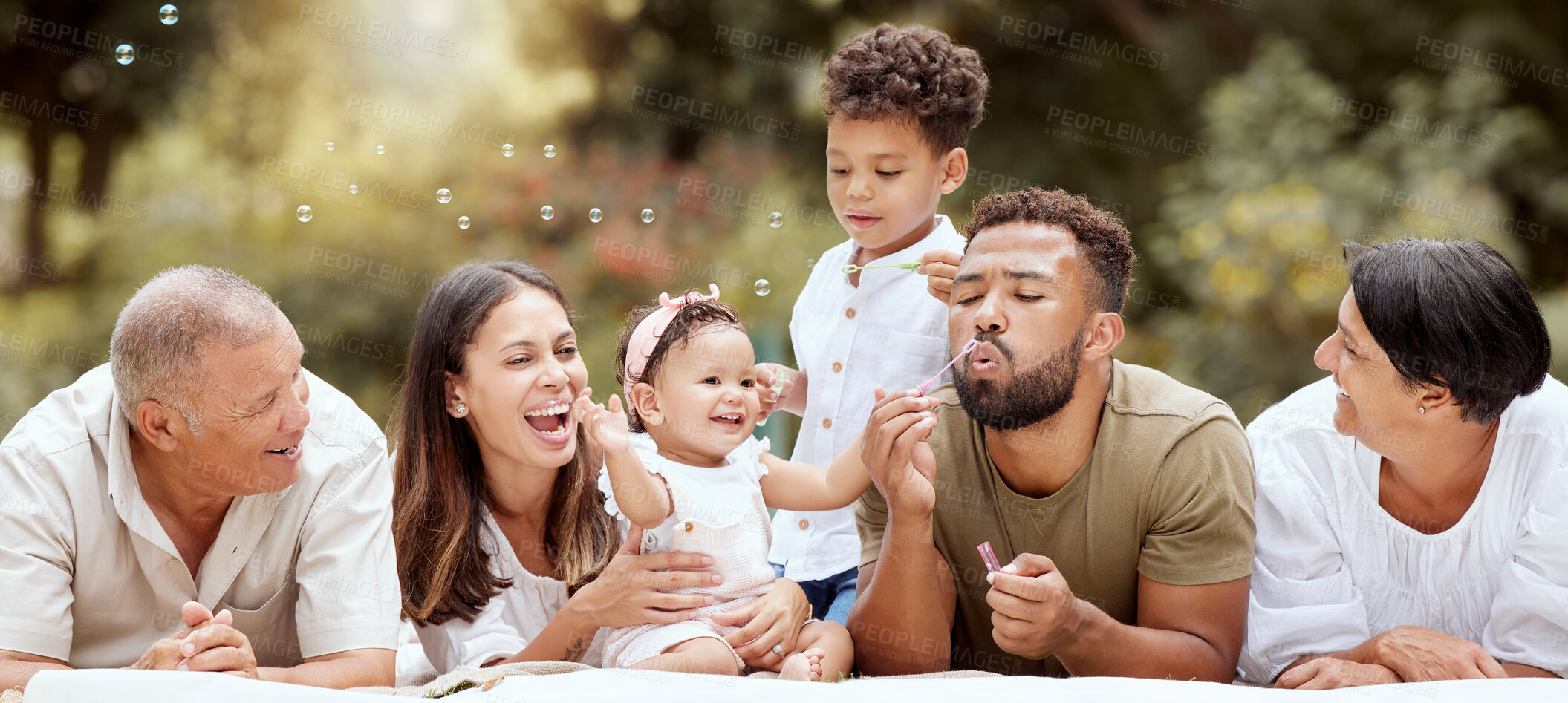 Buy stock photo Happy, smile and big family blowing bubbles in a garden on a summer picnic in Puerto Rico. Happiness, grandparents and parents with children playing, having fun and relaxing together in the park 