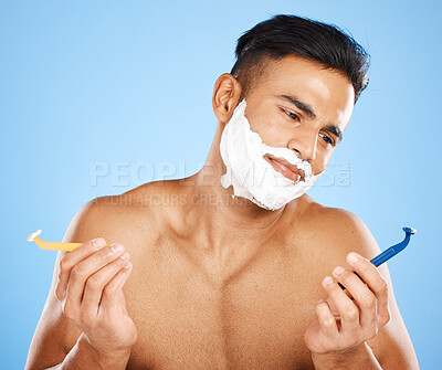 Buy stock photo Man, razor and shaving in studio for choice, confused or thinking of skin, cosmetics or performance. Model, shaving cream or blade for shave, grooming or skincare for hair on face by blue background