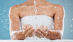 Water, splash and woman hands in a studio for hygiene, grooming or natural facial wash treatment. Skincare, wellness and girl cleaning or washing her face, skin or hand isolated by a blue background.
