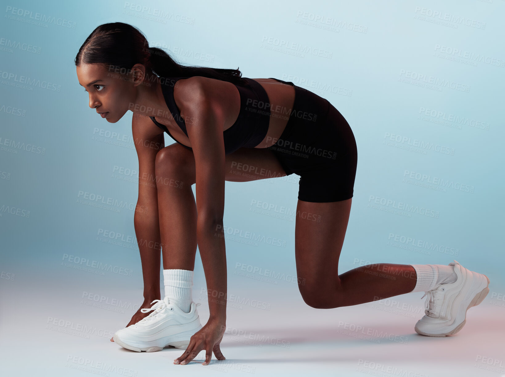 Buy stock photo Start position, runner and fitness woman in studio ready for marathon, exercise or cardio workout. Motivation, run and athlete or model from India doing sports training isolated by a blue background.