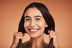 Portrait of woman holding hair for beauty, hairstyle and fashion isolated on orange background in studio. Beauty salon, smile and face of young female with healthy skin, wellness and hair products