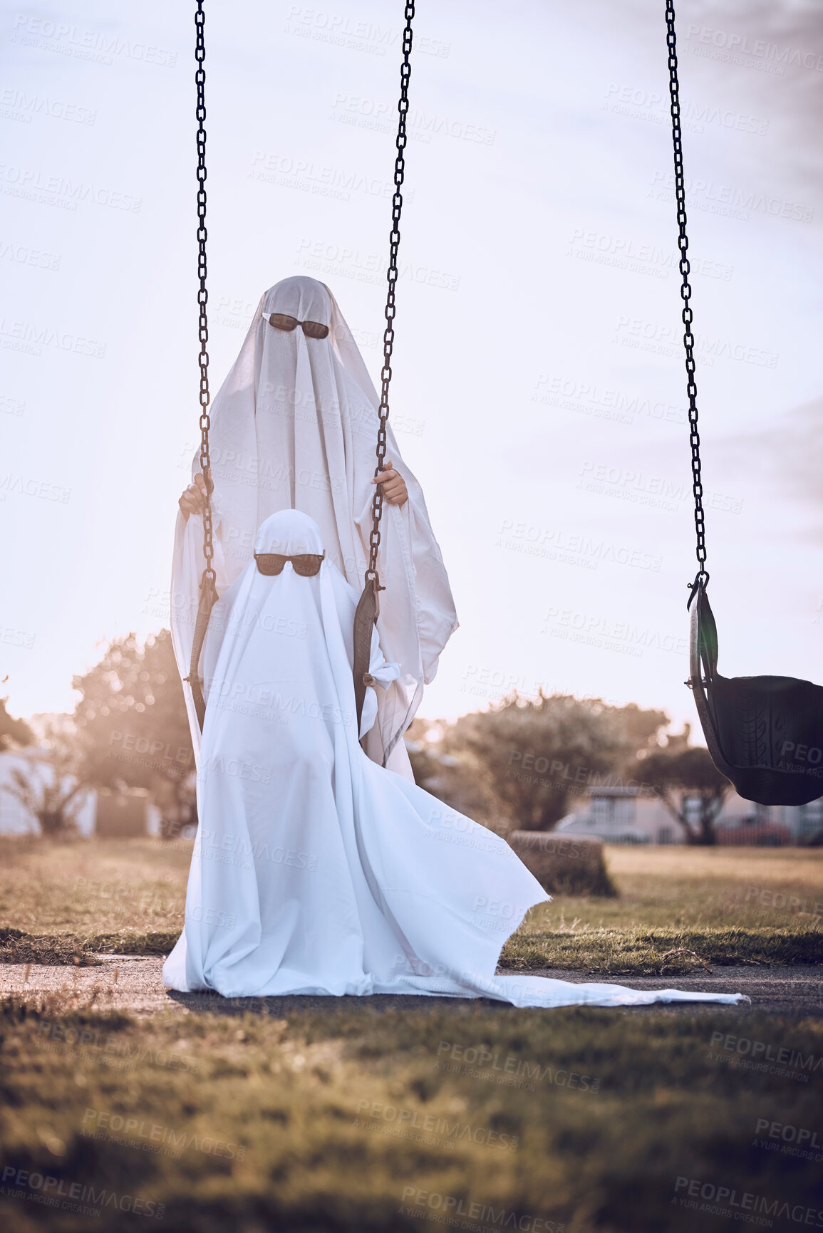 Buy stock photo Halloween, costume and ghost couple at park, kid enjoy scary holiday with parent. Family, festival and child with mom or dad in spooky white sheet dress up with sunglasses sitting on playground swing
