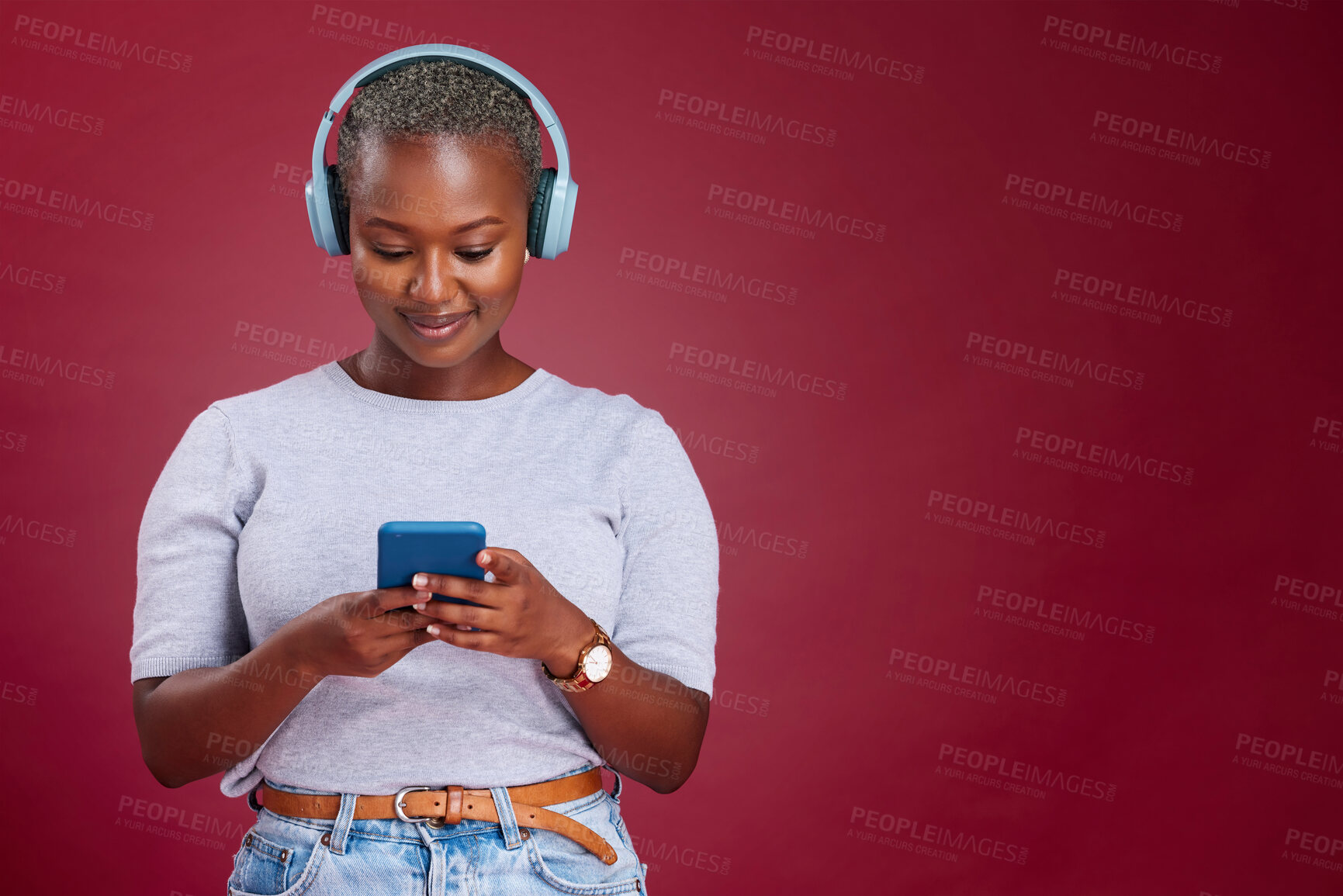 Buy stock photo Smartphone, headphone and black woman in studio mock up listening, scroll and typing on music subscription streaming service. African girl using phone audio app on red mockup marketing or advertising