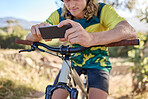 Hands, phone and mountain biking of man in sports cycling, fitness or exercise in the nature outdoors. Hand of male cyclist browsing, workout or checking online cycle training tours on smartphone