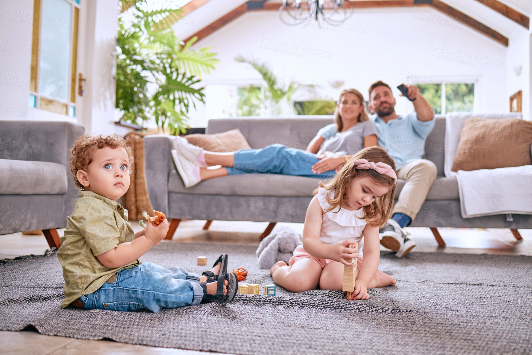 Buy stock photo Parents on sofa, children play on floor in home and family time together on weekend morning in Dallas. Streaming movie, young kids bonding with toys and dad searching channel watching tv with mom