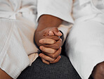 Closeup spa couple, holding hands and relax in bathrobe together at luxury resort for wellness treatment. Black couple sofa, support trust love and rest for health, care and calm for physical therapy