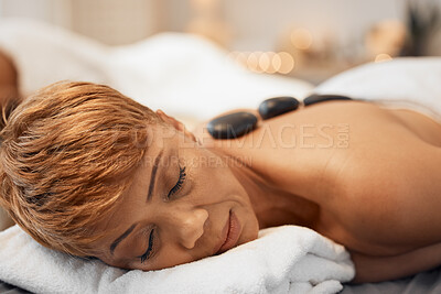 Buy stock photo Spa bed woman, hot stone massage and relax body, treatment and luxury physical therapy for wellness, health and stress. Black woman, rest salon and rock on back for healthcare, recovery or skincare
