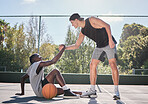 Sports, teamwork and men with helping hand in basketball, player giving support, help and assistance. Fitness, friends and man lifting black man with injury from ground on outdoor basketball court