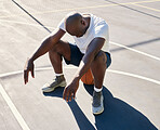 Basketball court, tired and black man sitting on a basketball resting or relaxing on a fitness training or workout break. Fatigue, wellness and African sports athlete after a cardio exercise outdoors