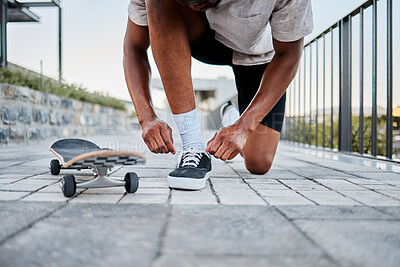 Buy stock photo Black man, shoes and skateboard, skater with shoelace in urban skate park for fitness, exercise and fun outdoor. Young person, cool and trendy out in nature, skating with sneakers and cityscape.