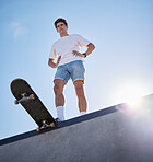 Blue sky, skateboard and young man from below on skate ramp ready for trick. Fitness, street fashion and urban sports, a skater in skatepark and summer sun for adventure, freedom and extreme sport.