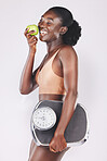 Happy woman, scales and apple for losing weight, healthy diet and fitness results, progress and exercise motivation on studio background. Black model eating fruits, sports nutrition and body wellness