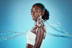 Skincare, water and black woman with a splash for hydration, cleaning and beauty against a blue studio background. Spa, wellness and African model with peace, calm and relax from liquid dermatology