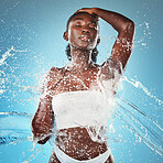 Woman, water splash and skincare body, beauty moisturiser or hydration by blue background wall. Black woman, skin model and splashes for cosmetics, health or dermatology wellness by cosmetic backdrop