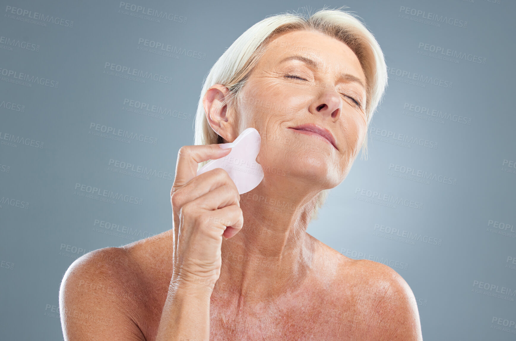 Buy stock photo Face, beauty and massage with a senior woman in studio on a gray background for skincare to relax. Skin, wellness and antiaging with a mature female using a massaging tool for natural treatment