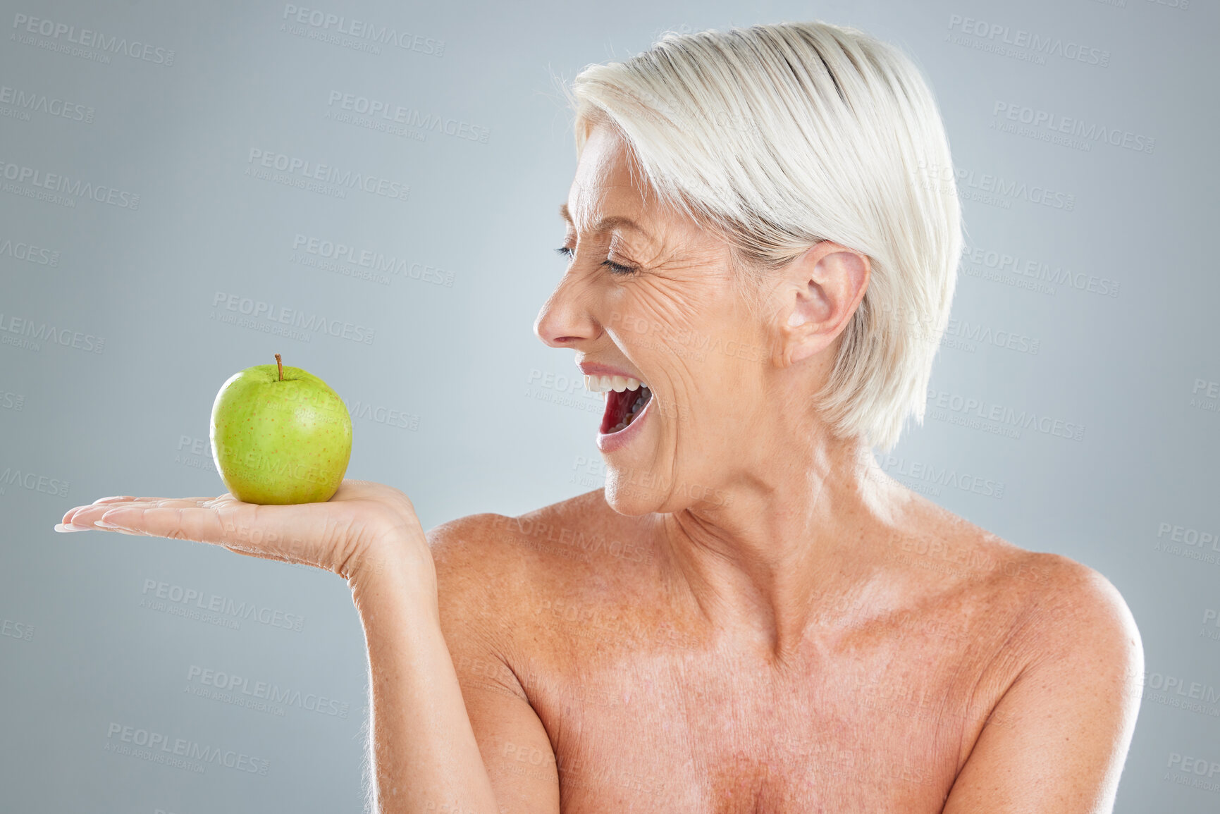 Buy stock photo Beauty, apple and excitement with a senior woman in studio on a gray background to promote healthy eating. Food, fruit and diet with a mature female posing for nutrition vitamins or health lifestyle