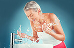 Beauty splash, senior and woman cleaning face in studio for wellness, skincare and hygiene on blue background mockup. Water splash, senior woman and happy, smile and water, beauty and skin facial