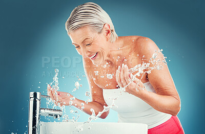 Buy stock photo Beauty splash, senior and woman cleaning face in studio for wellness, skincare and hygiene on blue background mockup. Water splash, senior woman and happy, smile and water, beauty and skin facial