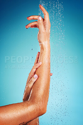 Buy stock photo Arm, water and person in the shower cleaning body against a blue studio background. Spa, wellness and hand of model woman with luxury hydration from liquid, dermatology and healthy care for skin 