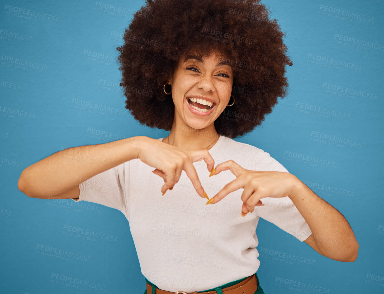 Buy stock photo Love, heart and woman with a smile for fashion, marketing and advertising against a blue mockup studio background. Excited, happy and portrait of a creative and African girl with emoji hands for care