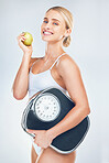 Health, diet and woman with scale and apple to lose weight for health, wellness and healthy lifestyle as fitness mockup studio background. Portrait, smile and body of model eating fruit for nutrition