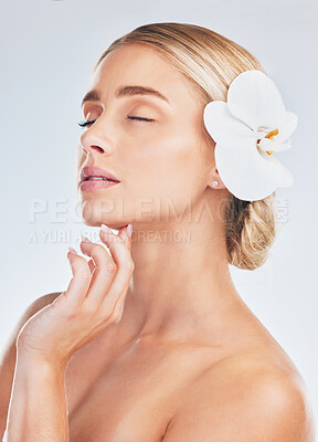 Buy stock photo Skincare, wellness and face of a woman with an orchid for health, beauty and dermatology against a grey studio background. Spa, flower and girl model with a natural plant for care for skin and body