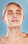 Water, skincare and face of a woman with a splash for cleaning, treatment and care against a blue studio background. Wellness, health and girl model with luxury facial dermatology to relax for beauty