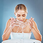 Face, water and cleaning with a model woman in studio on a blue background to wash her skin in the basin. Splash, skincare and hands with an attractive young female washing or cleansing in a bathroom