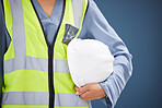 Closeup, construction worker and helmet with vest for safety in studio with blue background. Woman, builder and construction industry with gear, clothes and hardhat for health, wellness or protection