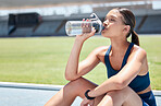 Tired, sports and drinking water woman with fitness training, exercise or workout at a stadium field for energy or motivation. Young athlete runner relax on ground or floor with water bottle gear