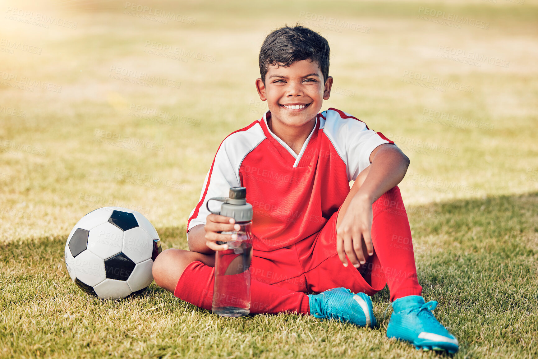 Buy stock photo Soccer, children and water with a ball and boy child sitting on a grass pitch or field after training. Football, fitness and hydration with a young male kid at a sports venue, stadium or arena