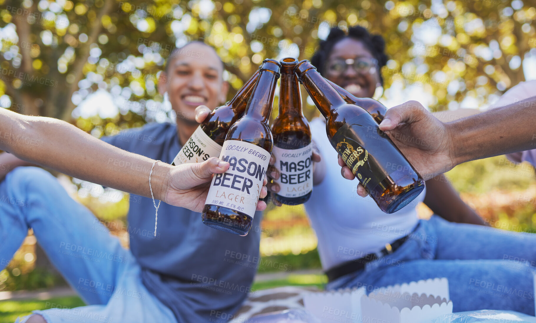 Buy stock photo Closeup, picnic and toast beer with friends on grass, happiness and together in nature, park or outdoor. Summer, happy time and diversity for cheers with bottle, craft beer and alcohol with people