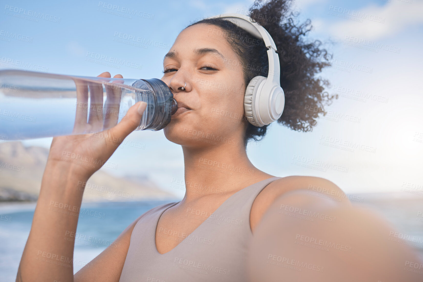 Buy stock photo Woman runner, drinking water and selfie with music while outdoor for exercise, workout or fitness. Black woman, headphones and beach for training, wellness or health in nature by ocean in summer sun