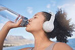 Fitness, headphone and woman drinking water after running, training and cardio workout at beach. Exercise, runner and thirsty with healthy liquid for hydrate, energy and wellness listening to music
