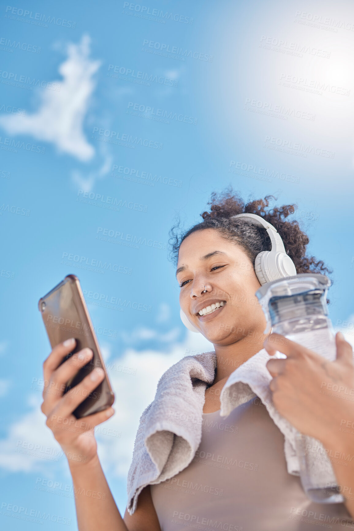 Buy stock photo Headphones, phone and woman with water bottle outdoors streaming music, radio or audio. Social media, networking and low angle of female on 5g mobile or text message after training or running workout