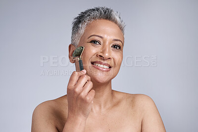 Buy stock photo Black woman, beauty and skincare with a facial roller or rose quartz in studio for cosmetics or dermatology product on grey background. Face portrait of a senior model with a smile for wellness glow