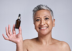 Senior woman, serum and skincare with smile for natural beauty, organic facial and wellness in grey studio background. Body care, model and with cosmetic oil for smooth skin, glow or happy to hydrate