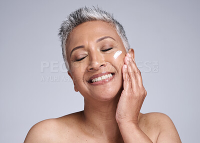 Buy stock photo Face, skincare and beauty with a senior woman using cream for antiaging treatment in studio on a gray background. Cosmetics, lotion and cosmetology with a mature female applying cream to skin