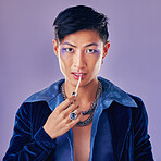 Fashion, beauty and makeup with a man model in studio on a purple background applying red lipstick. Face, portrait and cosmetics with a young asian male indoors to promote a cosmetic product