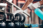 Kettlebell, cleaning service and hands cleaning at a gym with liquid soap in spray bottle with cloth in gloves. Janitor or cleaner wipes dirty bacteria on dusty weights or fitness training equipment