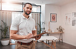 Wellness, health and happy physiotherapy portrait in professional workspace with notes clipboard. Rehabilitation, reflexology and expert therapy man in office for body trauma evaluation.


