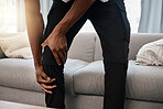 Black man, hands and knee injury in pain at home from accident, torn muscle or joint ache by living room sofa. African American male suffering from injured leg holding painful area, bruise or bone