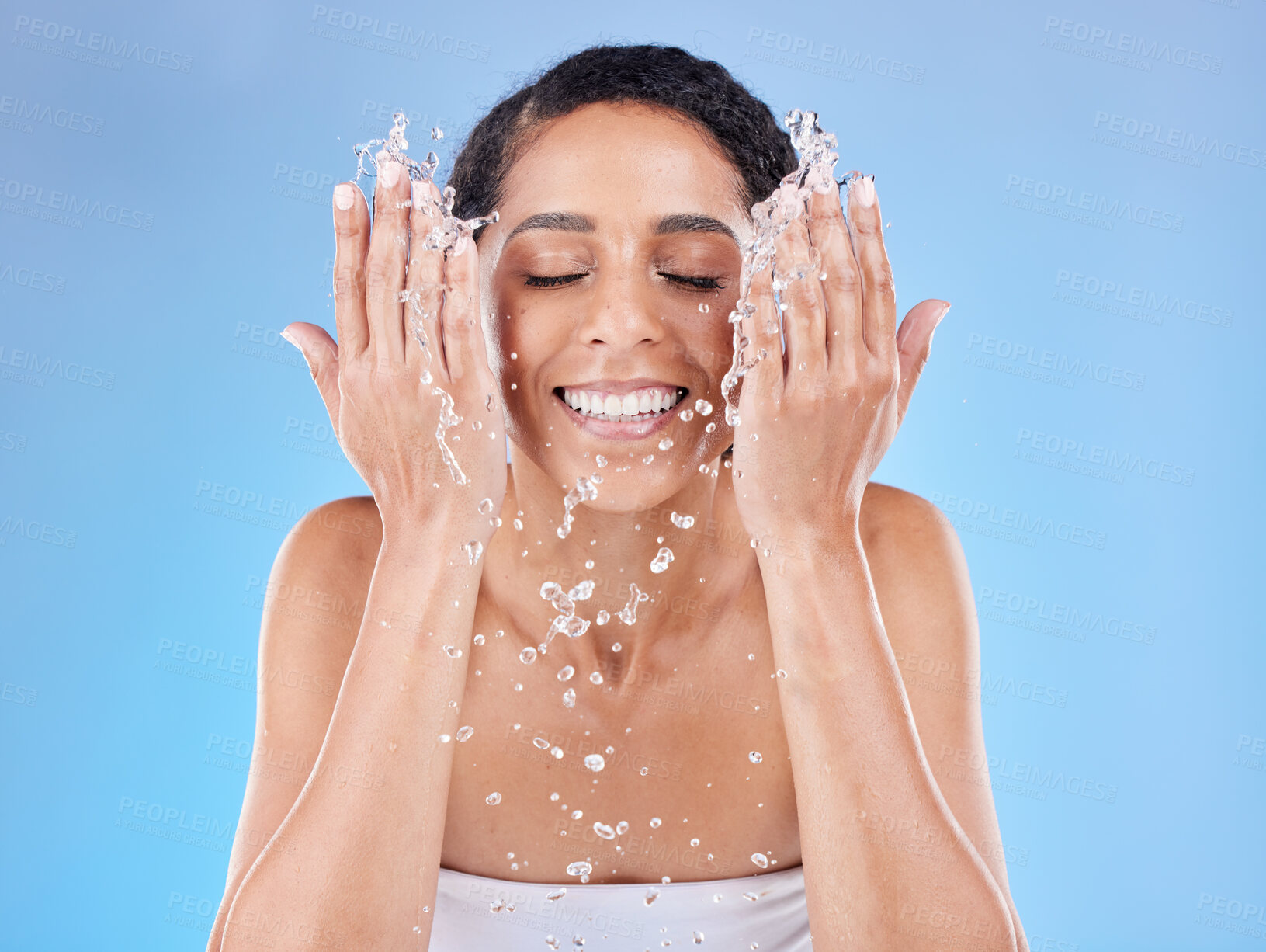 Buy stock photo Skincare, water and woman washing face for clean, healthy and natural wellness against a blue studio background. Beauty, cleaning and happy model with splash for facial satisfaction and routine