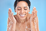 Water splash black woman cleaning face on blue background for health, beauty and skin care morning routine. Skincare, luxury cosmetics and happy woman with smile washing makeup with water in studio.