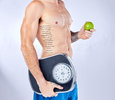 Buy stock photo Body, scale and apple with a man in studio on a gray background for weightloss, diet or healthy eating. Fitness, tattoo and health with a male holding fruit while posing for a nutrition lifestyle