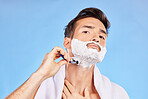 Portrait, shave and bathroom with a man model shaving his face in studio on a blue background for grooming. Beauty, skincare and shaving foam with a handsome young male using a razor in the morning